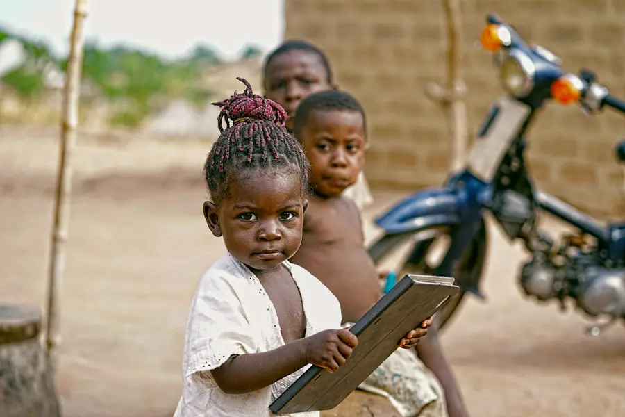 A girl holding a writing slate outside her home