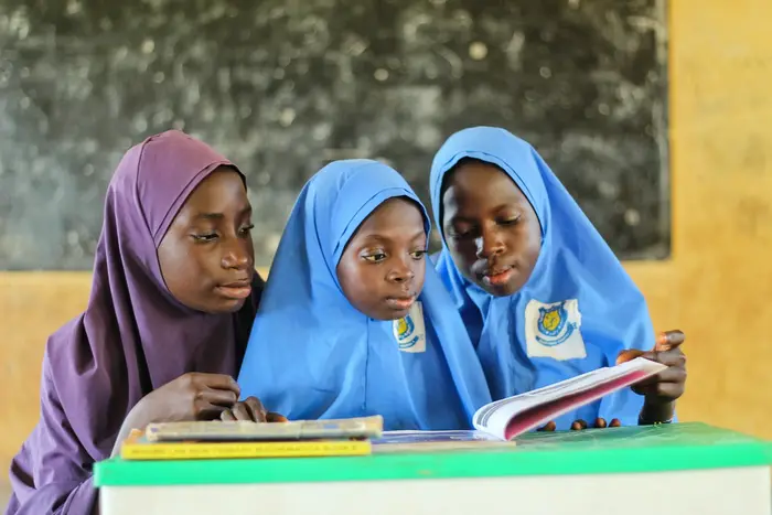Three schoolgirls reading a book together at a desk